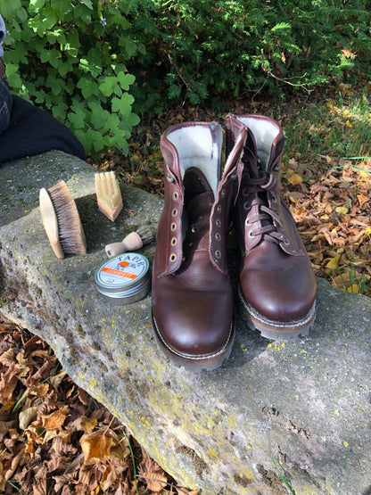 Braune Lederstiefel mit Tapir-Lederfett und Bürsten auf einem Stein im Freien