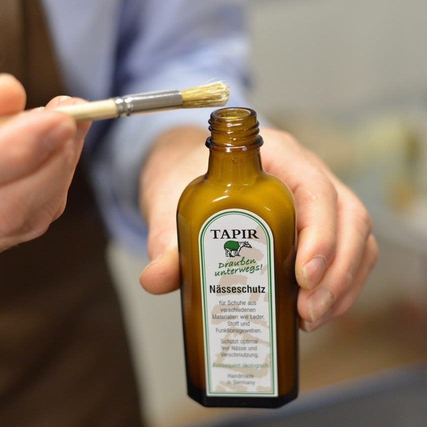 Tapir-Nässeschutz wird mit einem Pinsel aus der geöffneten Flasche aufgenommen